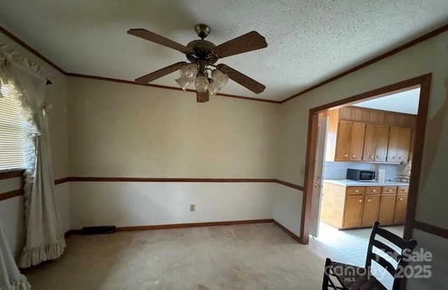 interior space with ceiling fan, light colored carpet, ornamental molding, and a textured ceiling