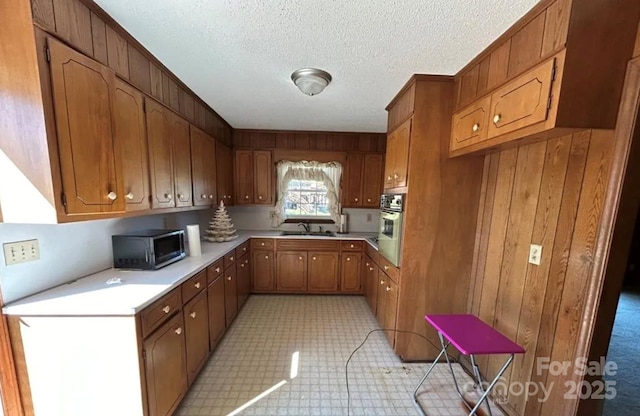 kitchen with wooden walls, oven, sink, and a textured ceiling