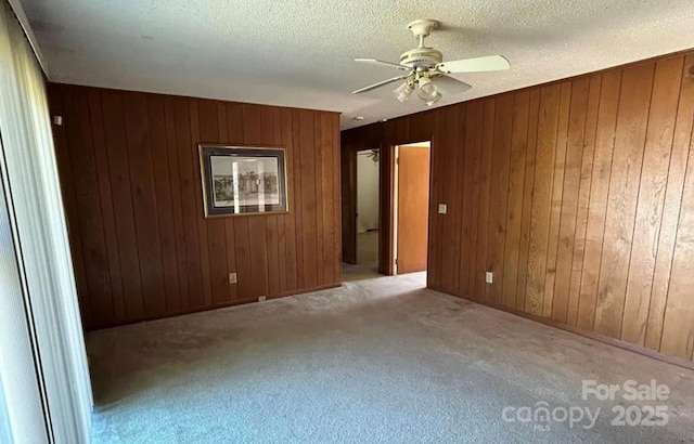 unfurnished room with light carpet, a textured ceiling, wooden walls, and ceiling fan