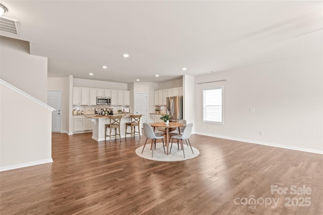 dining space with baseboards, wood finished floors, visible vents, and recessed lighting