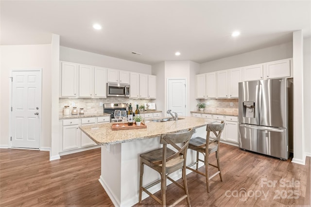 kitchen with wood finished floors, a sink, stainless steel appliances, backsplash, and white cabinetry