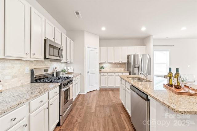kitchen featuring an island with sink, backsplash, a sink, appliances with stainless steel finishes, and white cabinetry