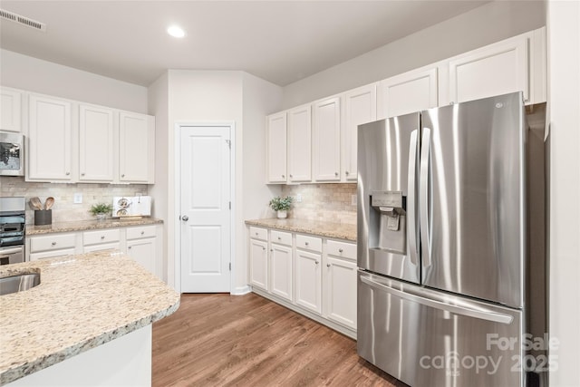kitchen with recessed lighting, light wood finished floors, decorative backsplash, appliances with stainless steel finishes, and white cabinetry