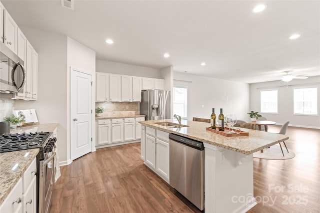 kitchen with a sink, light wood-type flooring, decorative backsplash, appliances with stainless steel finishes, and white cabinetry
