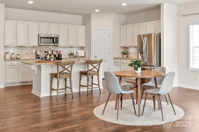 kitchen featuring decorative backsplash, an island with sink, appliances with stainless steel finishes, white cabinets, and dark wood-style flooring