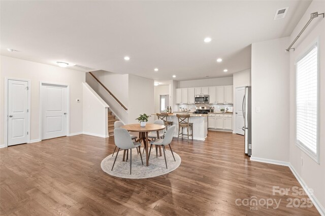 dining area featuring baseboards, wood finished floors, visible vents, and stairs