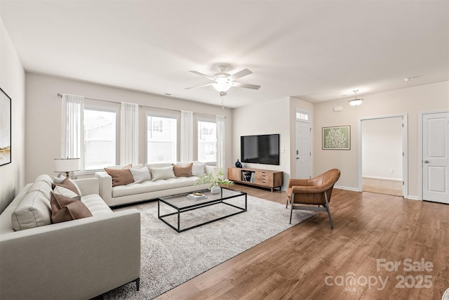 living room featuring ceiling fan, baseboards, and wood finished floors