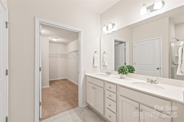 full bathroom with a walk in closet, baseboards, a sink, and double vanity