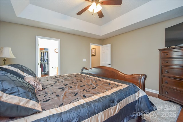 bedroom featuring a walk in closet, wood-type flooring, a raised ceiling, and ceiling fan