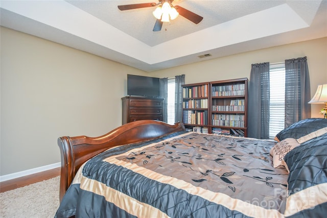 bedroom with hardwood / wood-style floors, a textured ceiling, a raised ceiling, and ceiling fan