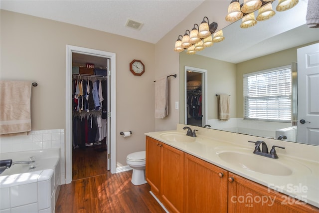 bathroom with hardwood / wood-style floors, vanity, a textured ceiling, a tub to relax in, and toilet