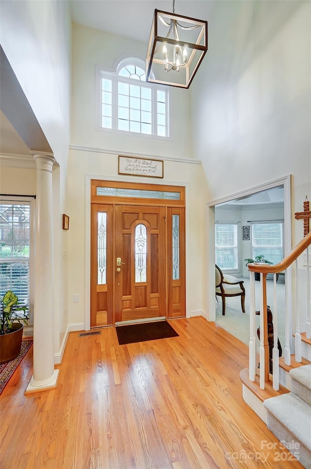 entryway with a high ceiling, stairway, light wood-type flooring, and decorative columns