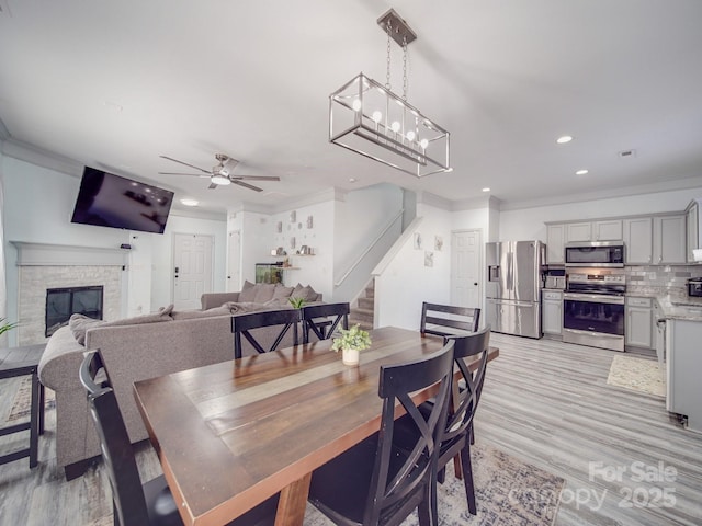 dining room with ornamental molding, ceiling fan, a fireplace, and light hardwood / wood-style floors