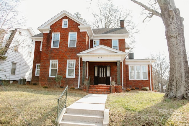 view of front of property featuring cooling unit, brick siding, a chimney, and a front yard