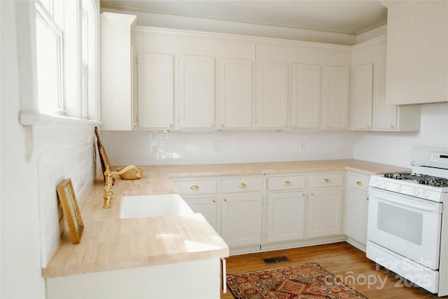 kitchen with white cabinets, white gas range, light countertops, light wood-type flooring, and a sink