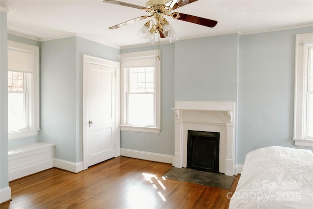 bedroom featuring ornamental molding, multiple windows, wood finished floors, and baseboards