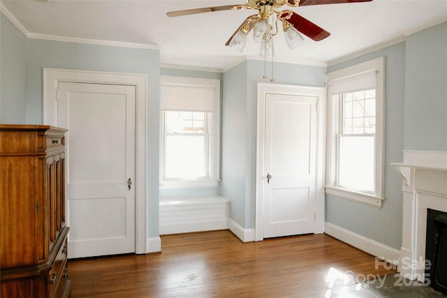 unfurnished living room with a fireplace with flush hearth, ornamental molding, baseboards, and wood finished floors