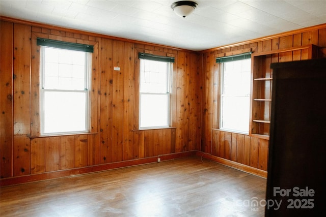 spare room featuring wood walls, baseboards, and wood finished floors