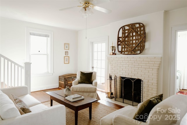 living area with a brick fireplace, a ceiling fan, and wood finished floors