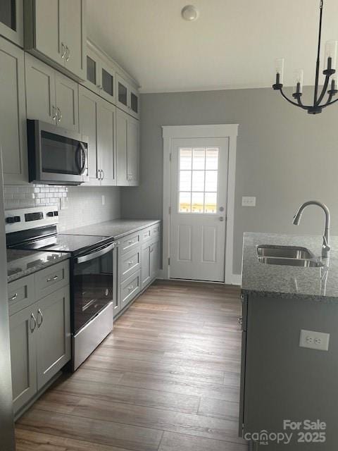 kitchen with sink, light stone counters, stainless steel appliances, light hardwood / wood-style floors, and decorative backsplash