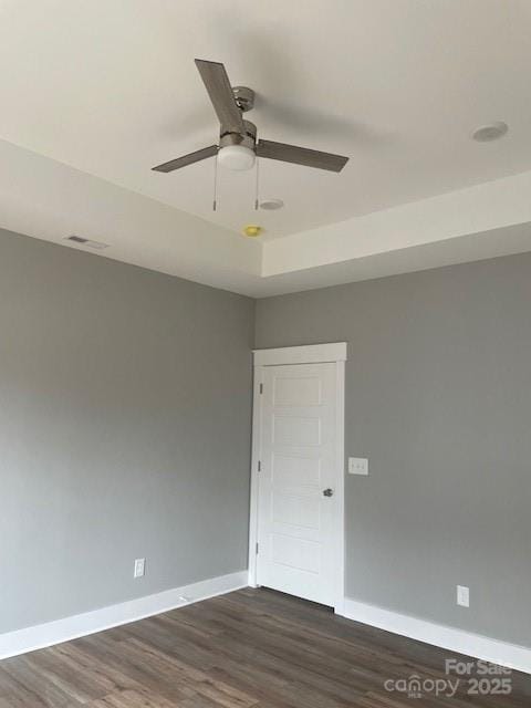 empty room with a tray ceiling, dark wood-type flooring, and ceiling fan