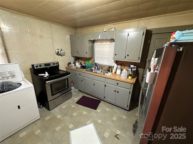 kitchen featuring washer / dryer, butcher block countertops, sink, gray cabinetry, and stainless steel appliances