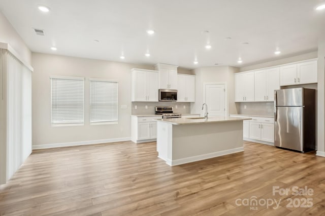 kitchen with white cabinetry, sink, stainless steel appliances, a center island with sink, and light hardwood / wood-style flooring