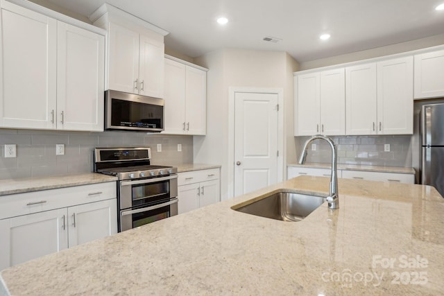 kitchen featuring stainless steel appliances, white cabinetry, light stone countertops, and sink