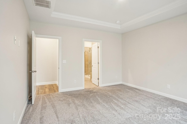 unfurnished bedroom featuring ornamental molding, connected bathroom, light colored carpet, and a tray ceiling