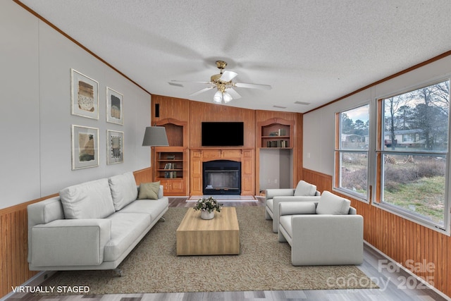 living room featuring crown molding, a healthy amount of sunlight, a textured ceiling, and wood walls