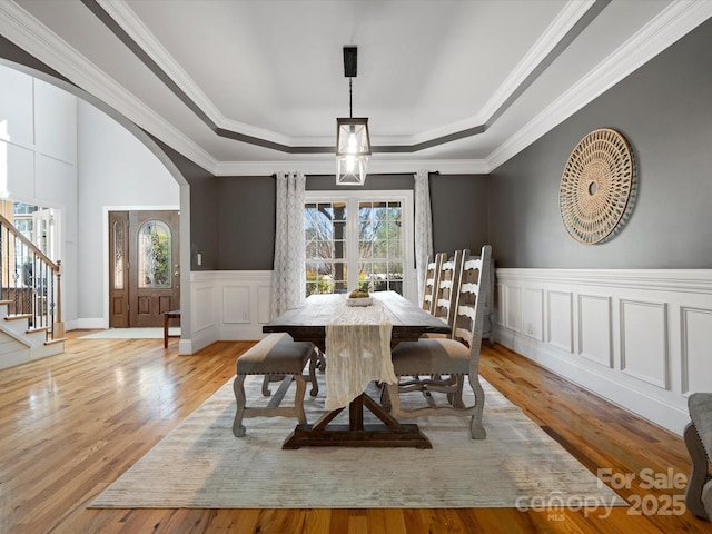 dining room with a tray ceiling, a wainscoted wall, arched walkways, and wood finished floors