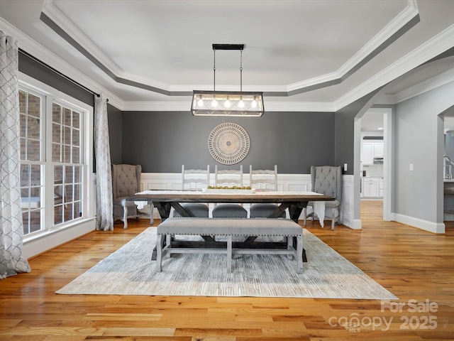 dining room featuring a tray ceiling, arched walkways, and wainscoting