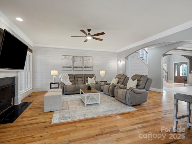 living room with arched walkways, a fireplace with flush hearth, stairway, wood finished floors, and crown molding