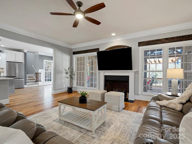 living area with ornamental molding, a fireplace with flush hearth, light wood-style flooring, and baseboards