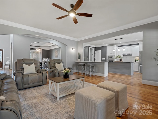 living room featuring arched walkways, ornamental molding, baseboards, and light wood-style floors