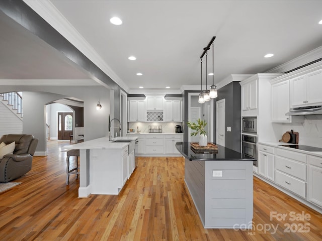 kitchen with arched walkways, a breakfast bar area, under cabinet range hood, a sink, and appliances with stainless steel finishes