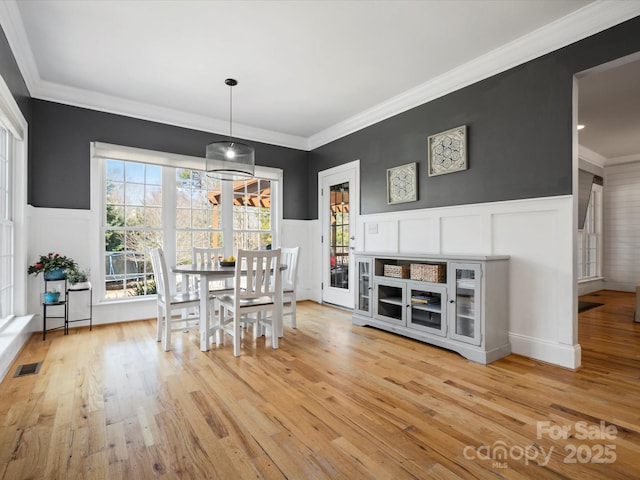 dining room featuring a wainscoted wall, ornamental molding, visible vents, and light wood-style floors