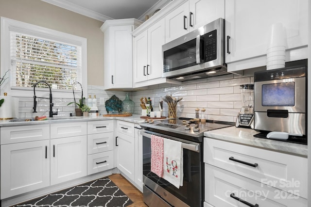 kitchen with white cabinetry, sink, ornamental molding, light stone counters, and stainless steel appliances