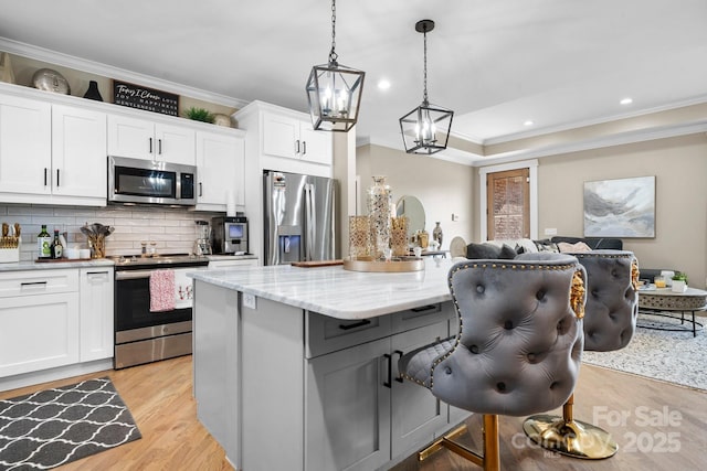 kitchen featuring hanging light fixtures, stainless steel appliances, a center island, light stone countertops, and white cabinets