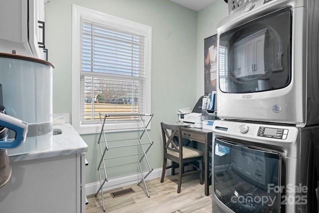 laundry room with stacked washer and clothes dryer, a wealth of natural light, and light hardwood / wood-style flooring