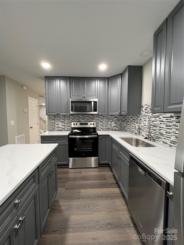 kitchen with dark wood-type flooring, sink, gray cabinetry, tasteful backsplash, and appliances with stainless steel finishes