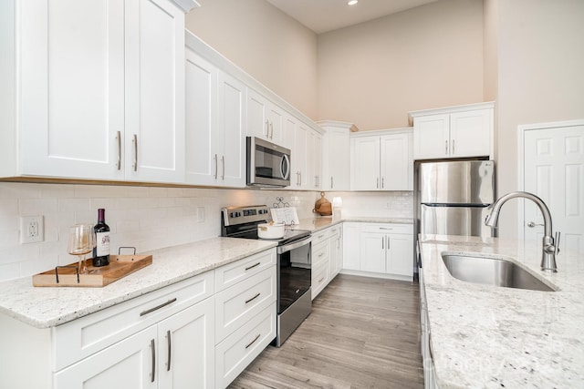 kitchen featuring sink, white cabinetry, stainless steel appliances, light stone countertops, and a high ceiling