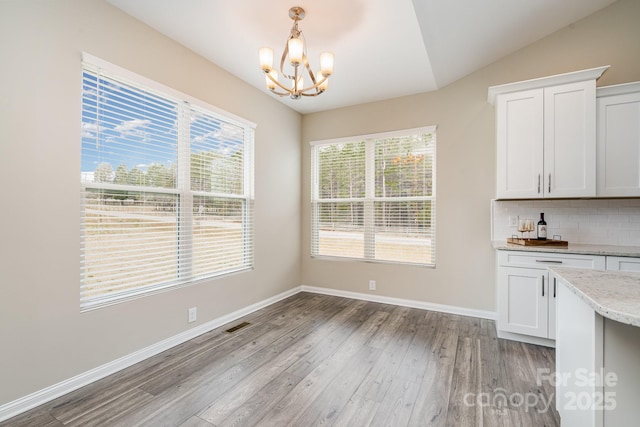 unfurnished dining area with vaulted ceiling, a notable chandelier, and light hardwood / wood-style flooring