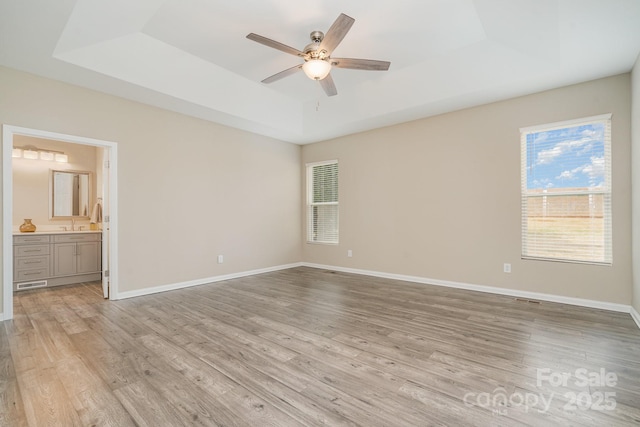 unfurnished room featuring a raised ceiling, ceiling fan, and light hardwood / wood-style floors