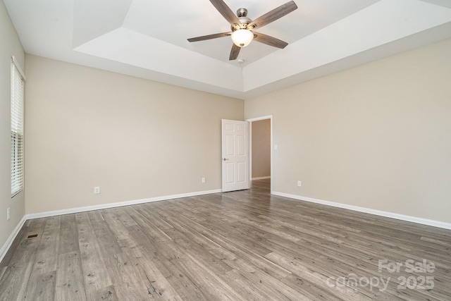 empty room with a tray ceiling, wood-type flooring, and ceiling fan