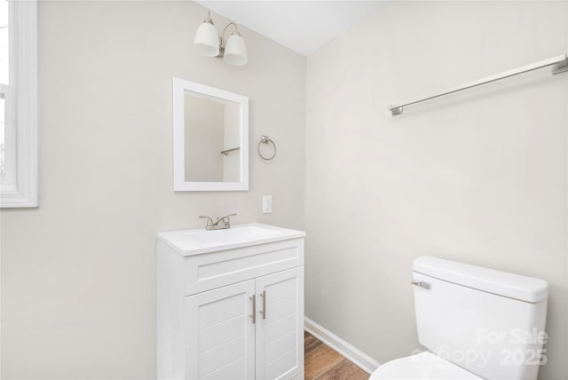 half bath featuring toilet, baseboards, wood finished floors, and vanity