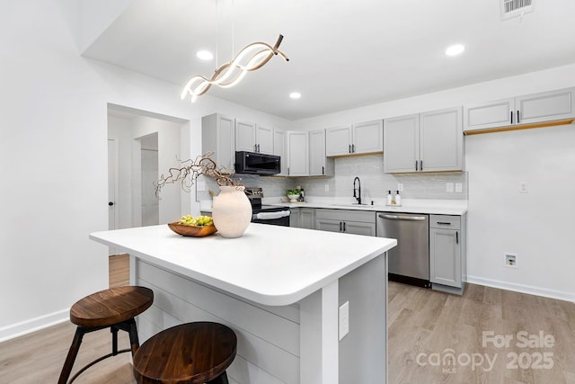 kitchen with decorative light fixtures, gray cabinets, stainless steel appliances, light hardwood / wood-style floors, and decorative backsplash