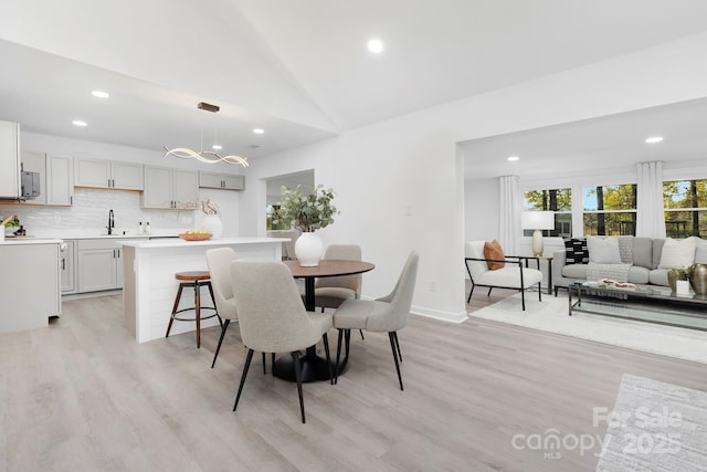 dining area with lofted ceiling, sink, and light hardwood / wood-style floors