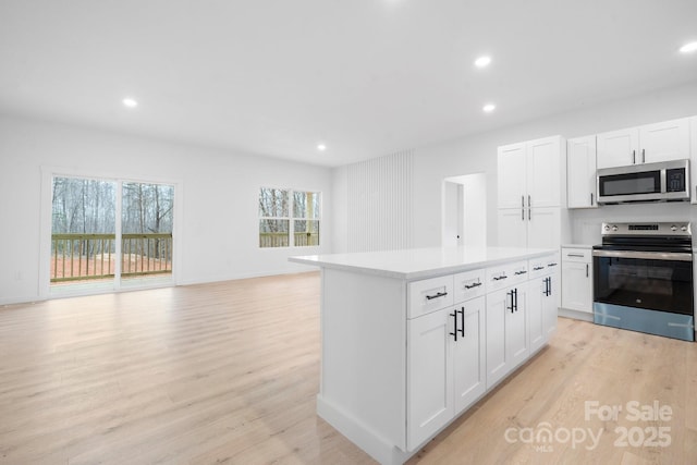 kitchen with light wood-style flooring, open floor plan, a center island, stainless steel appliances, and light countertops