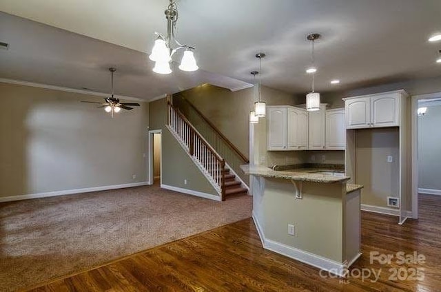 kitchen featuring a breakfast bar, kitchen peninsula, pendant lighting, light stone countertops, and white cabinets